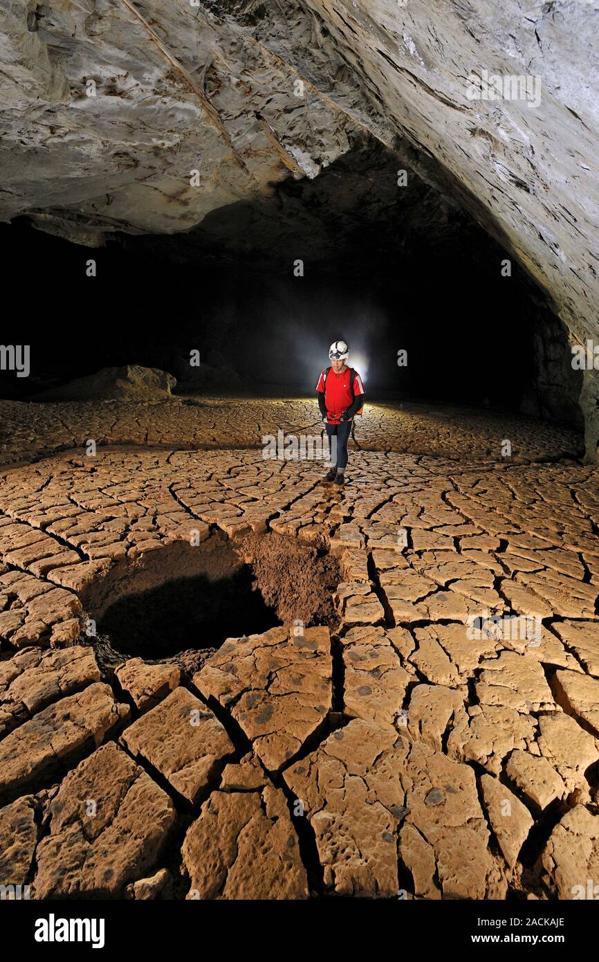 Cave mud floor. Cave explorer examining a hole in the cracked mud floor