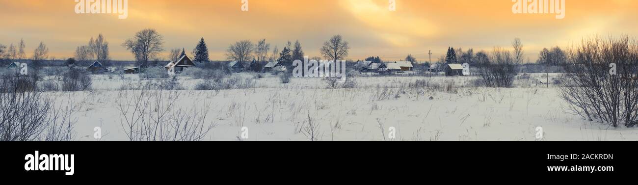 Winter panorama with beautiful sunset over the russian village and the snow-covered field under an orange sky Stock Photo