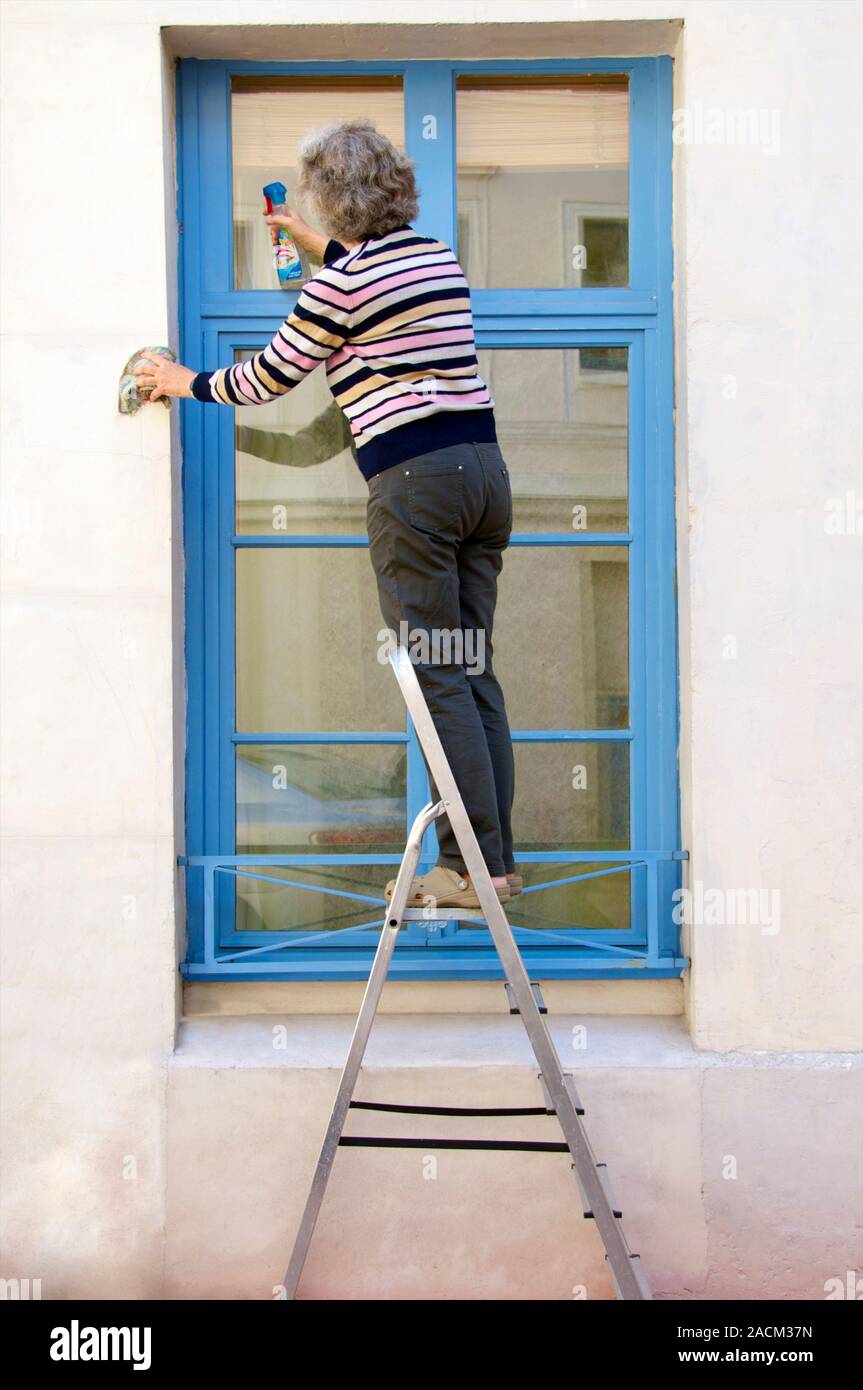 Window cleaning. Woman using a step-ladder while cleaning windows. Stock Photo
