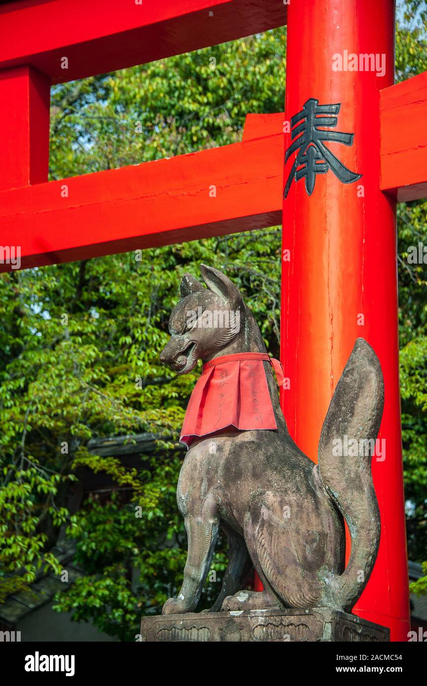 Kitsune (fox) statue wearing a red bib and holding a scroll in it's