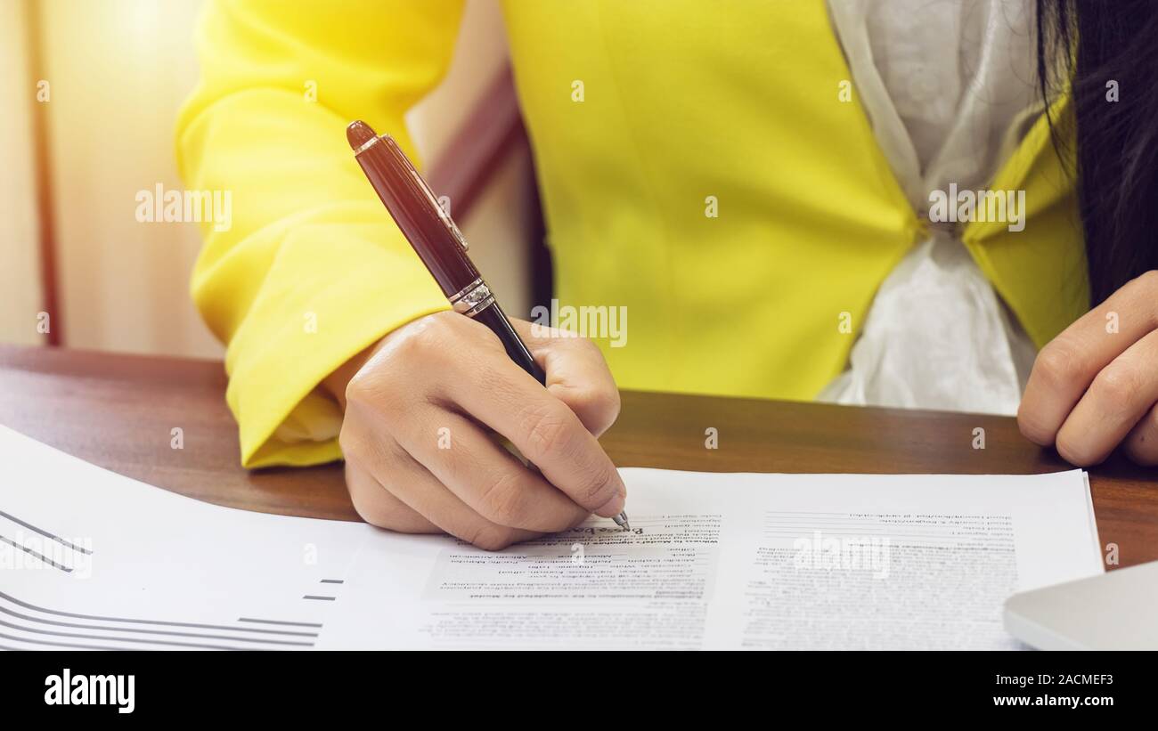business women in yellow suite use pen sign the signature of consent in the contract agreement document. business partnership and legal agreement of l Stock Photo
