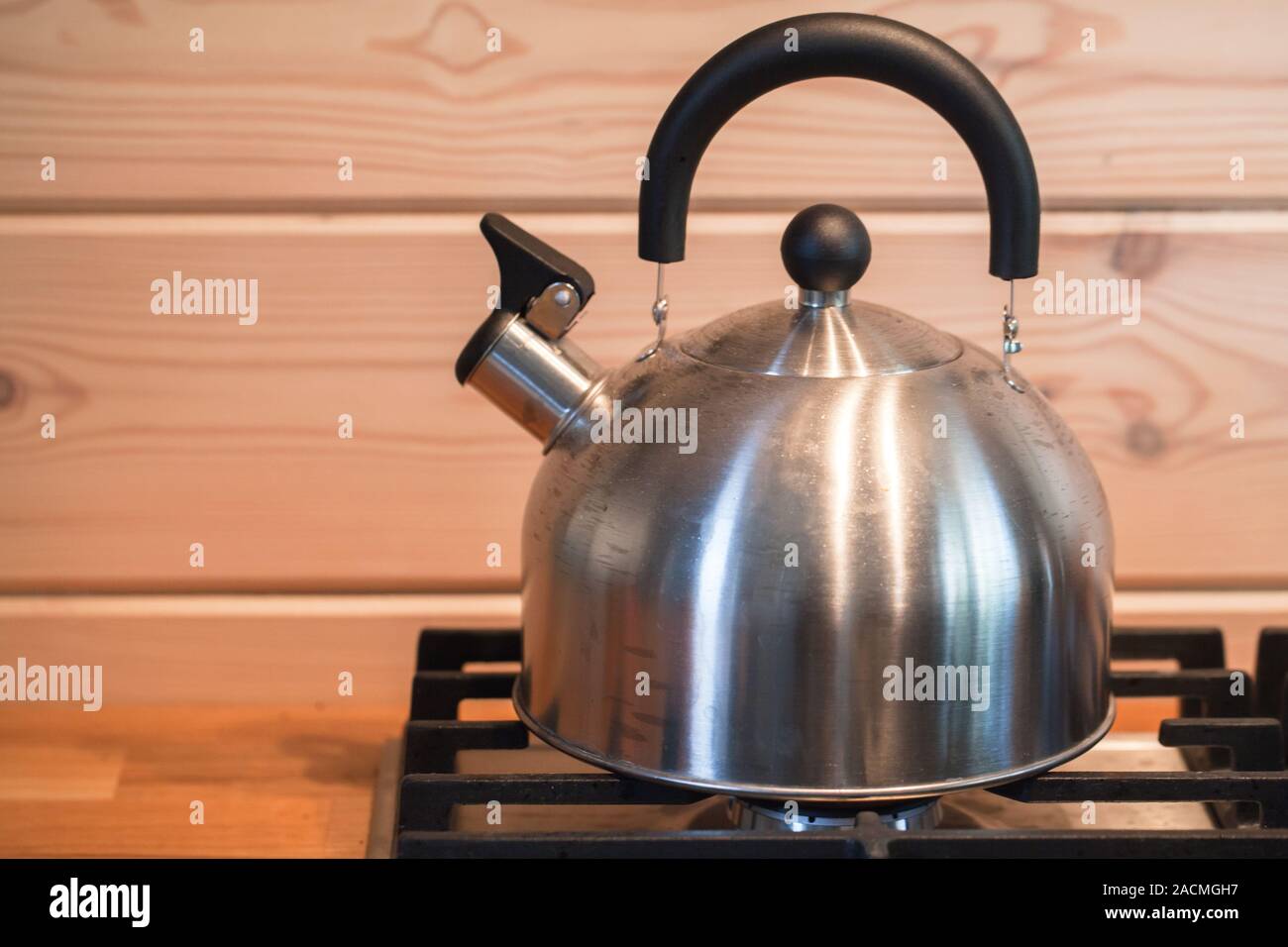 Stainless steel whistle kettle stands on a gas stove with wooden wall