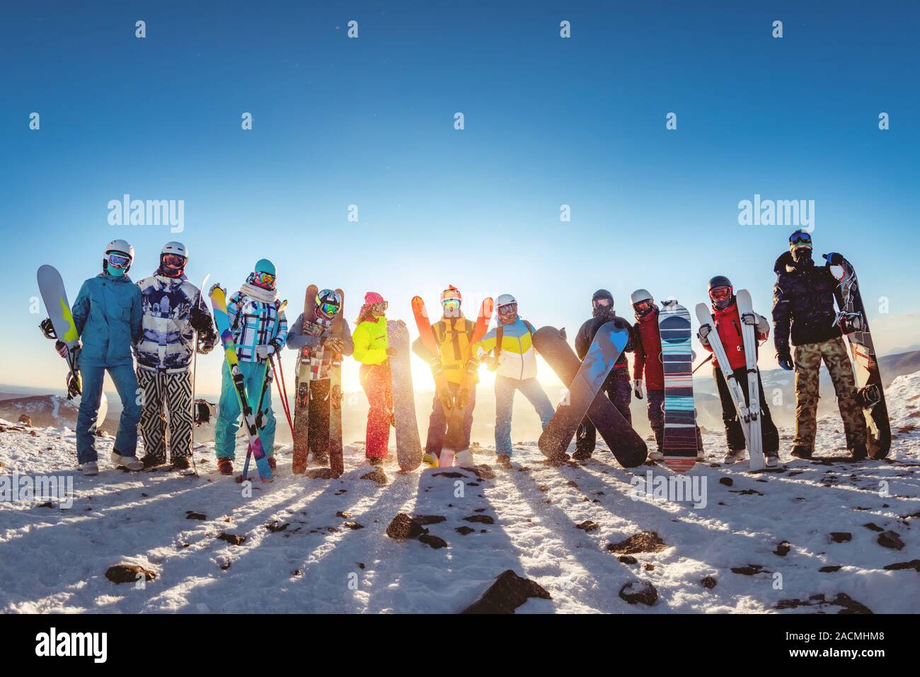 Big group of friends skiers and snowboarders are posing with equipment at sunset mountain Stock Photo