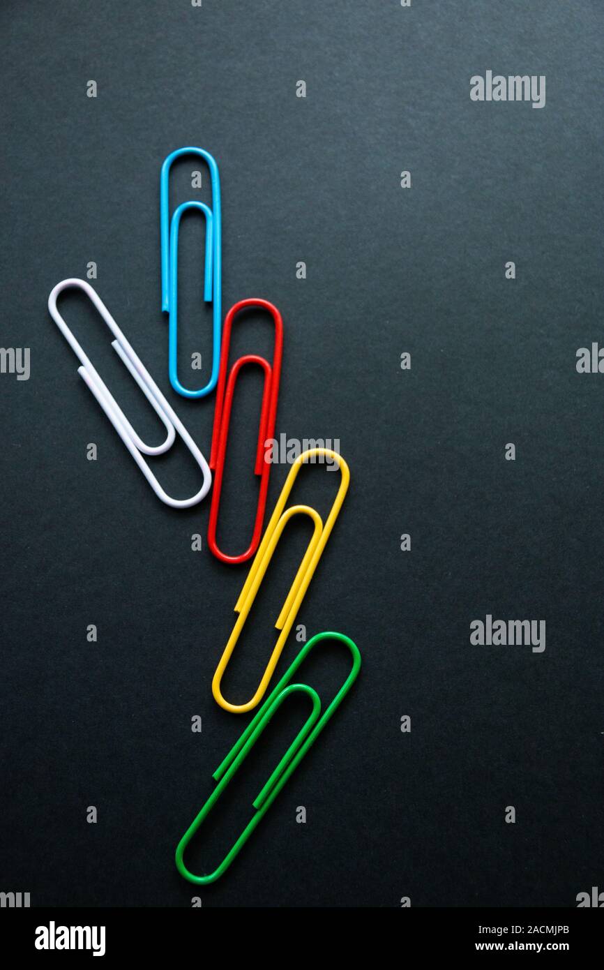 multi-colored paper clips on dark background, stationery. Stock Photo
