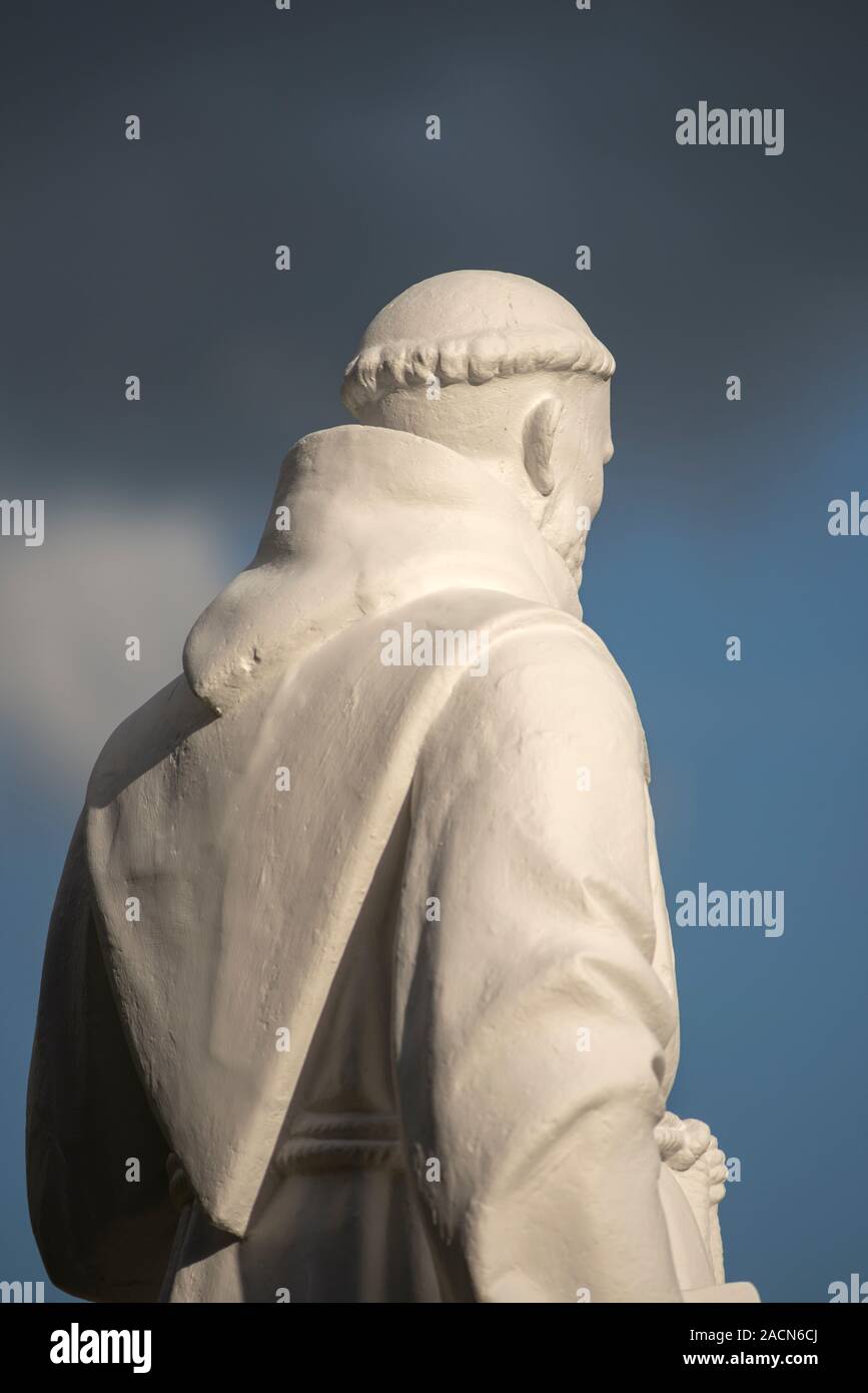 Religious figure statue of a mysterious friar monk back wearing Franciscan habit robe against dramatic sky. Stock Photo