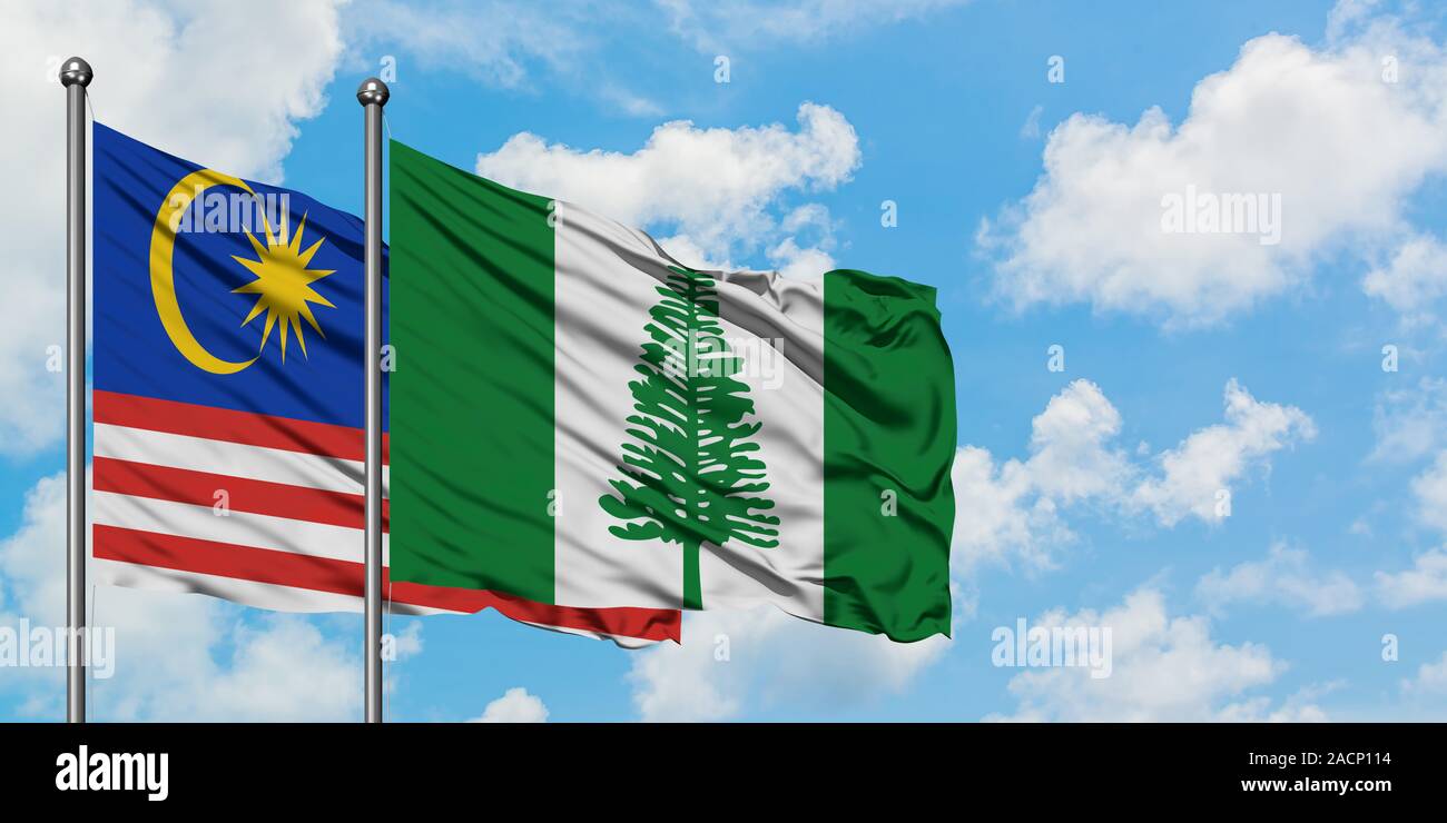Malaysia and Norfolk Island flag waving in the wind against white cloudy blue sky together. Diplomacy concept, international relations. Stock Photo