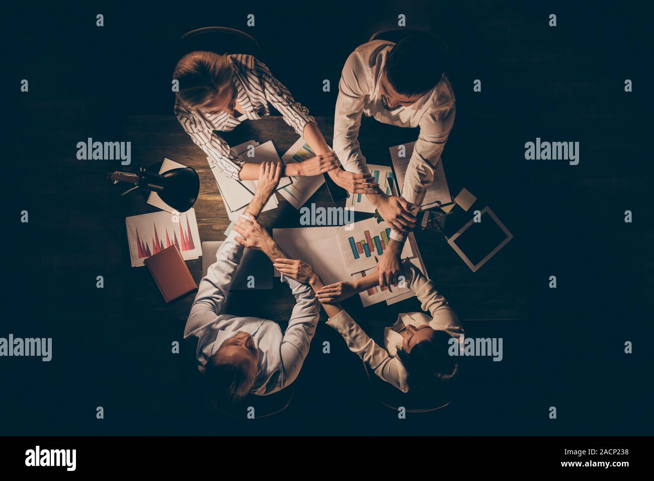 Top above high angle view of four hardworking people executive managers partners leaders shaking hands gathering over table desk at late night Stock Photo