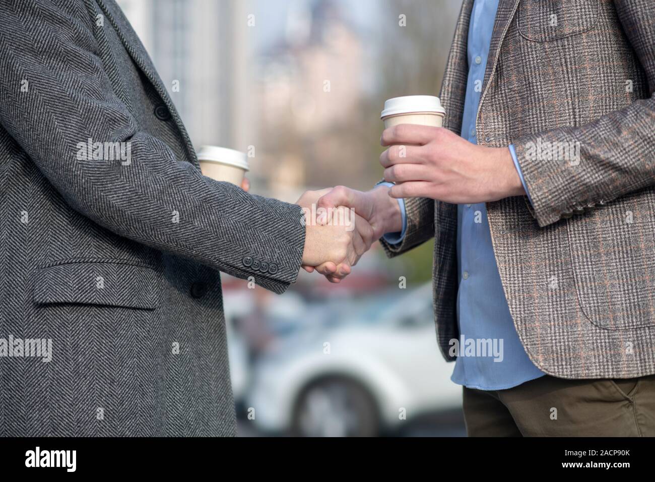 Two men with coffee cups shaking each others hand Stock Photo