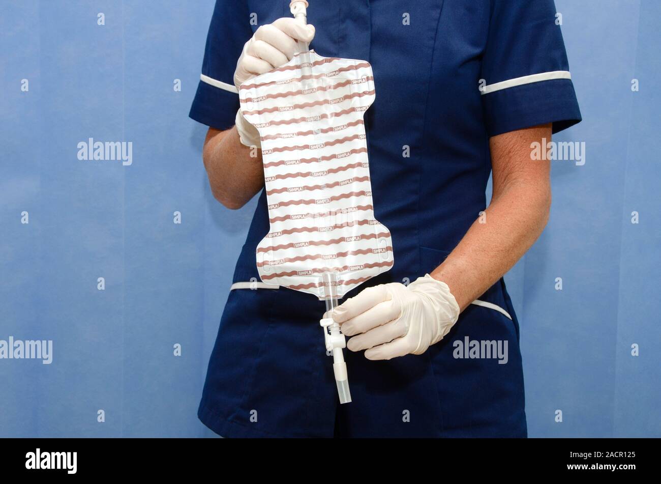 Gloved hands hold a sterile urinary catheter bag (leg bag), into which