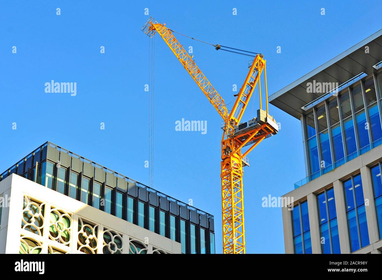 Bright yellow crane above and between two modern office blocks in Machester city centre Stock Photo