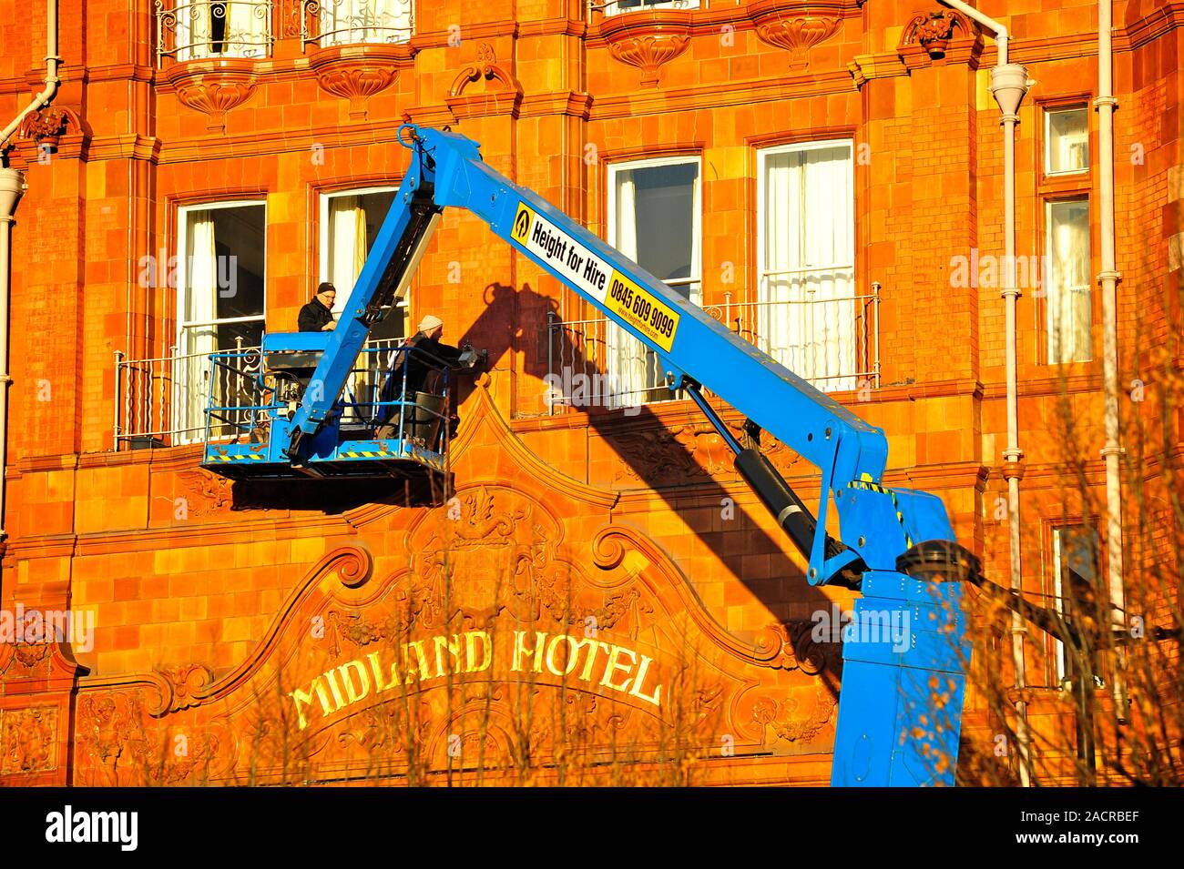 Two men on a hydraulic platform working on the front of the Midland Hotel in bright late afternoon winter sunshine,Manchester,UK Stock Photo