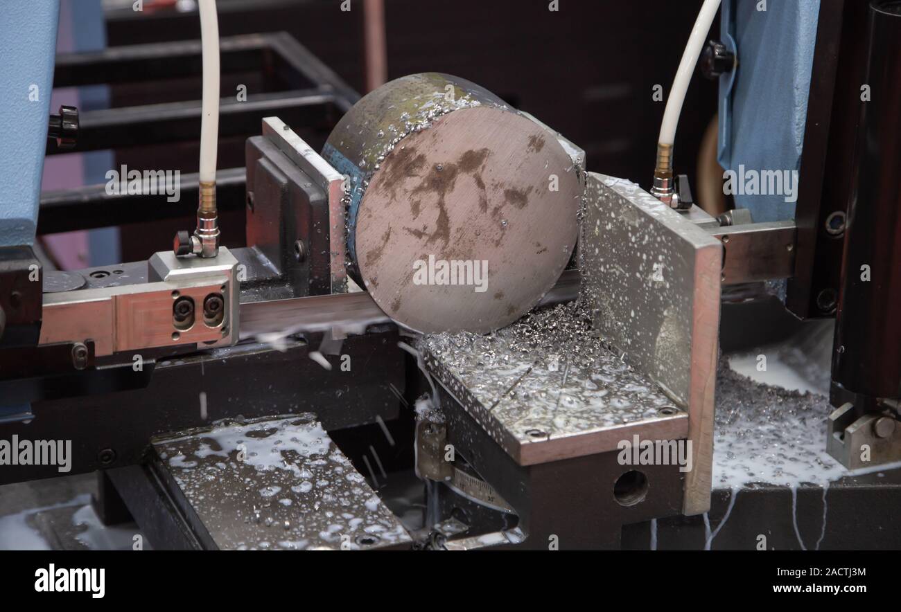 Band saw machine cutting metal rod and cooling with coolant Stock Photo