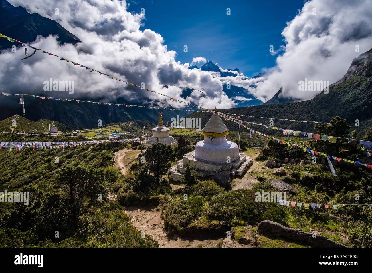 Buddhist stupas on a mountain slope above town, Mt. Thamserku covered in monsoon clouds in the distance Stock Photo