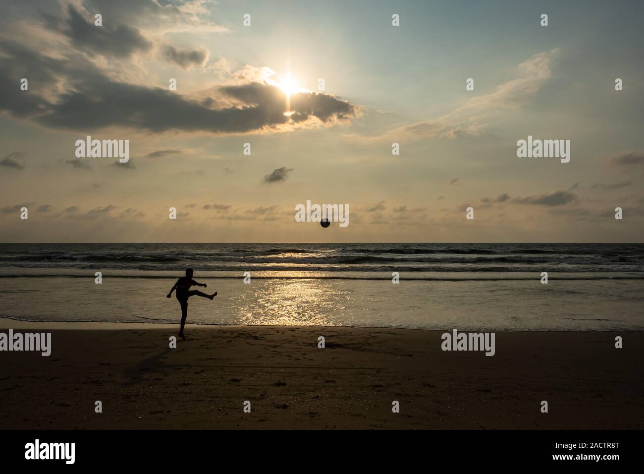 A boy kicking a ball at sunset on Benaulim Goa beach Stock Photo