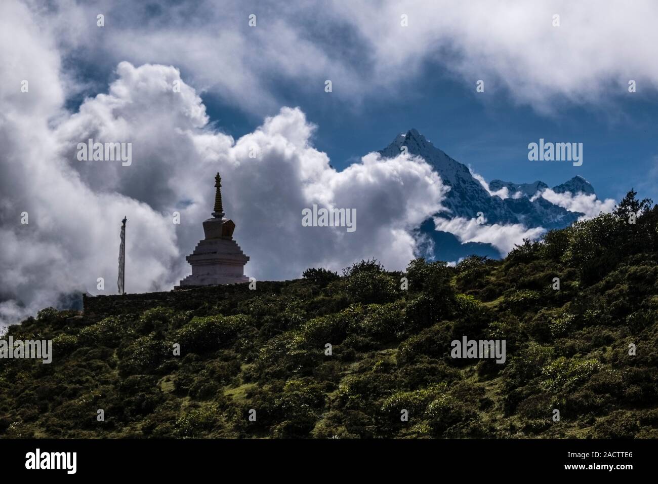 Buddhist stupa on a mountain slope above town, Mt. Thamserku covered in monsoon clouds in the distance Stock Photo