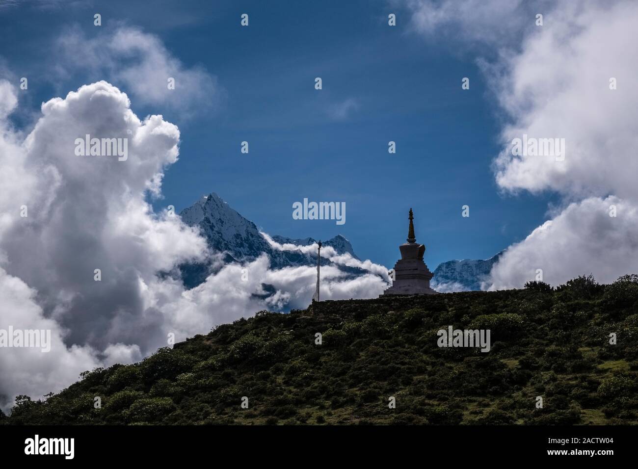 Buddhist stupa on a mountain slope above town, Mt. Thamserku covered in monsoon clouds in the distance Stock Photo