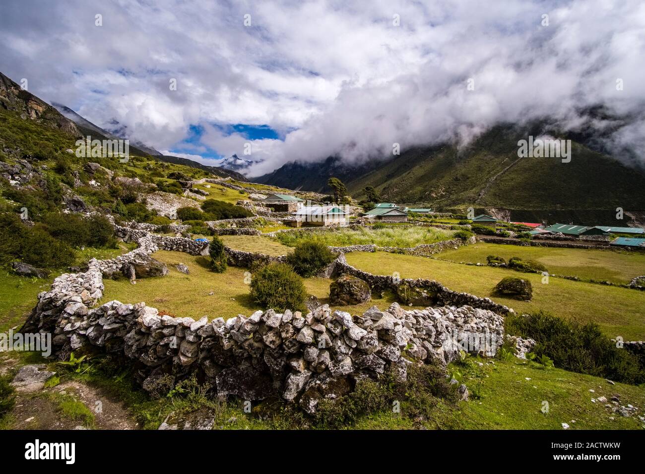 The fields of the small village are surrounded by stone walls, mountainous landscape covered in monsoon clouds in the distance Stock Photo