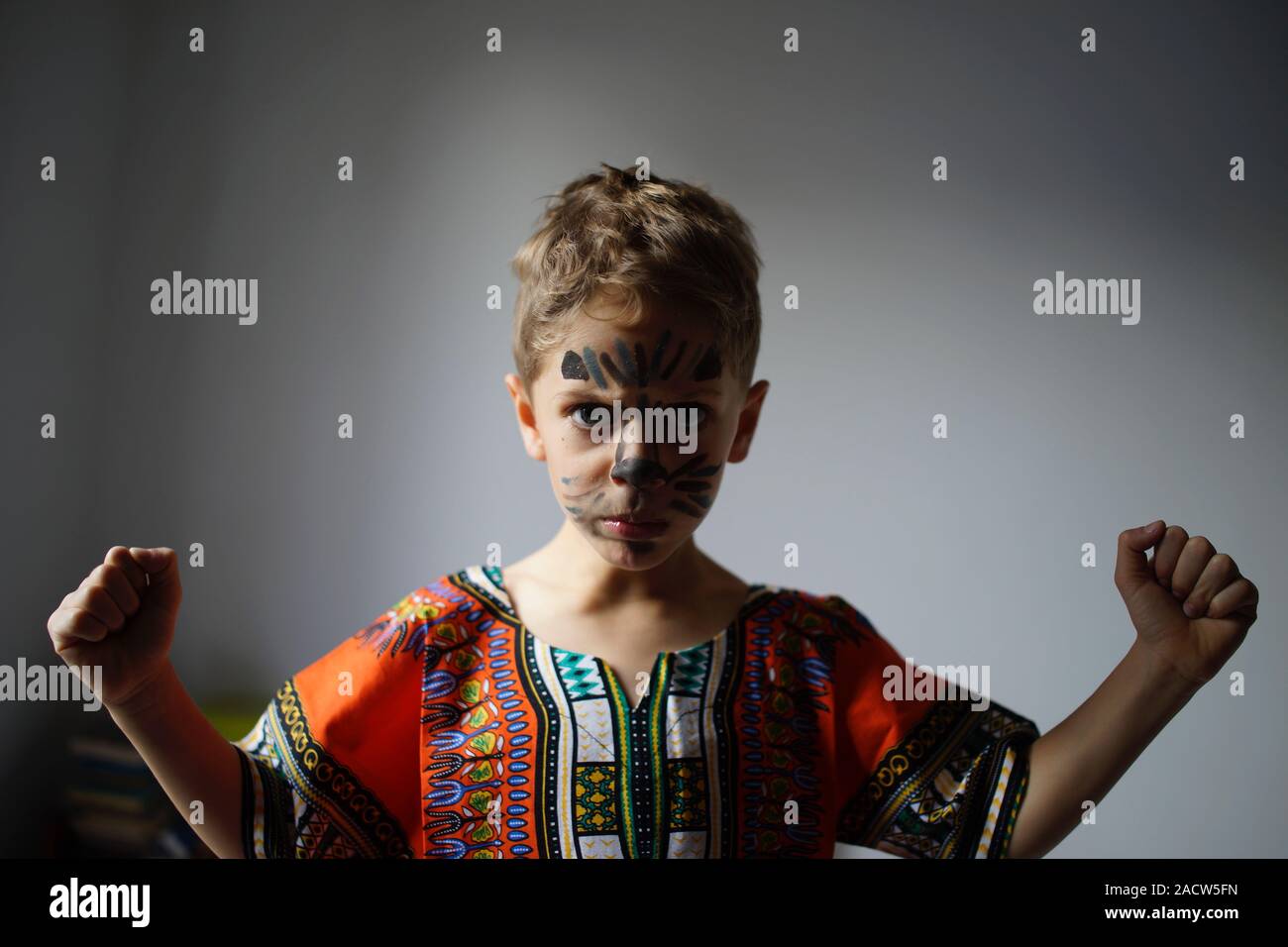 Boy with painted face and raised fists, raised wearing traditional African Dashiki shirt Stock Photo