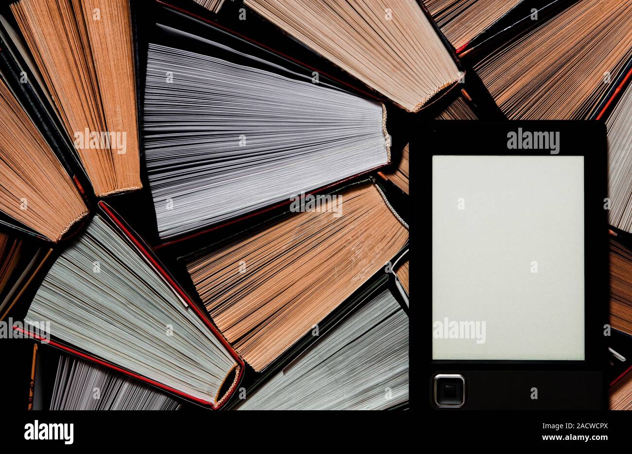 The e-book with a clean white screen rests on the open multi-colored books. ready to read Stock Photo