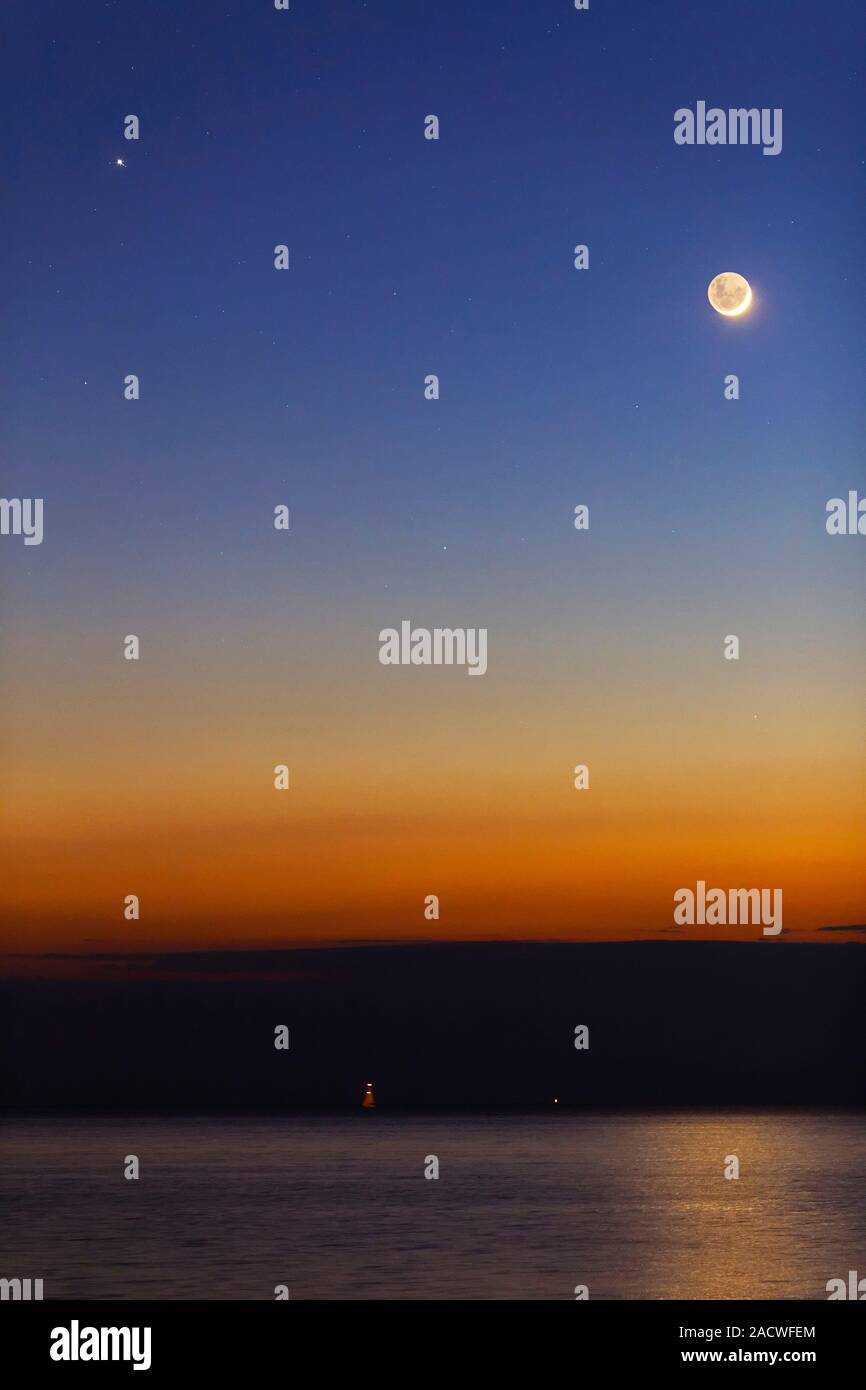 Moon with Jupiter, Mars and Mercury. The crescent Moon (upper right) is seen above the glow of the rising Sun on the horizon. Three planets are visibl Stock Photo