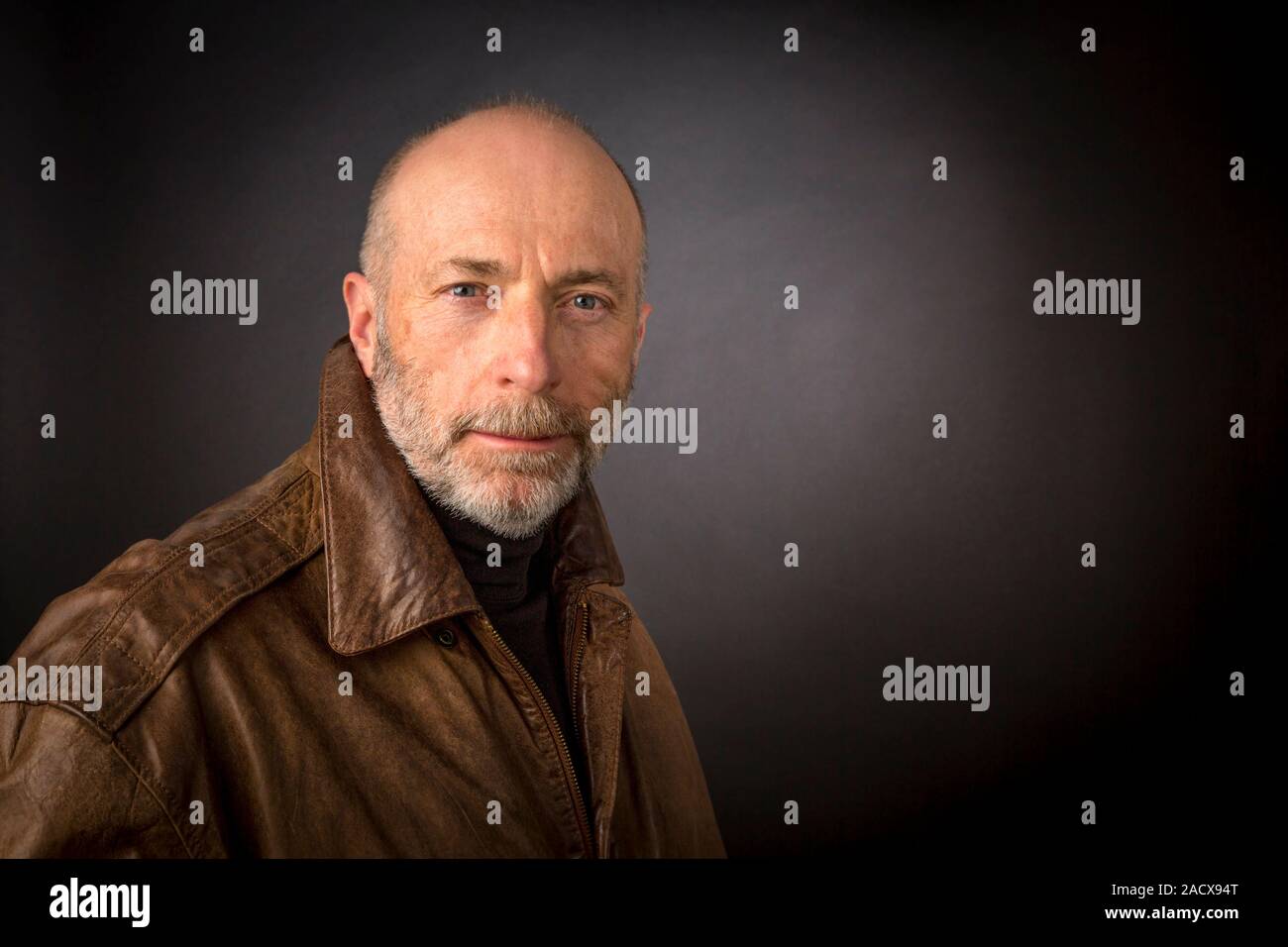 confident smirking senior man in leather jacket - an authentic headshot against a dark background Stock Photo