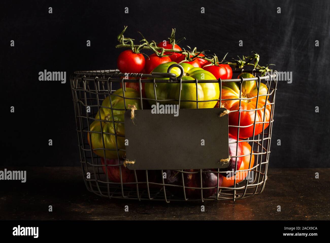 Different tomatoes in a wire basket on a dark background Stock Photo