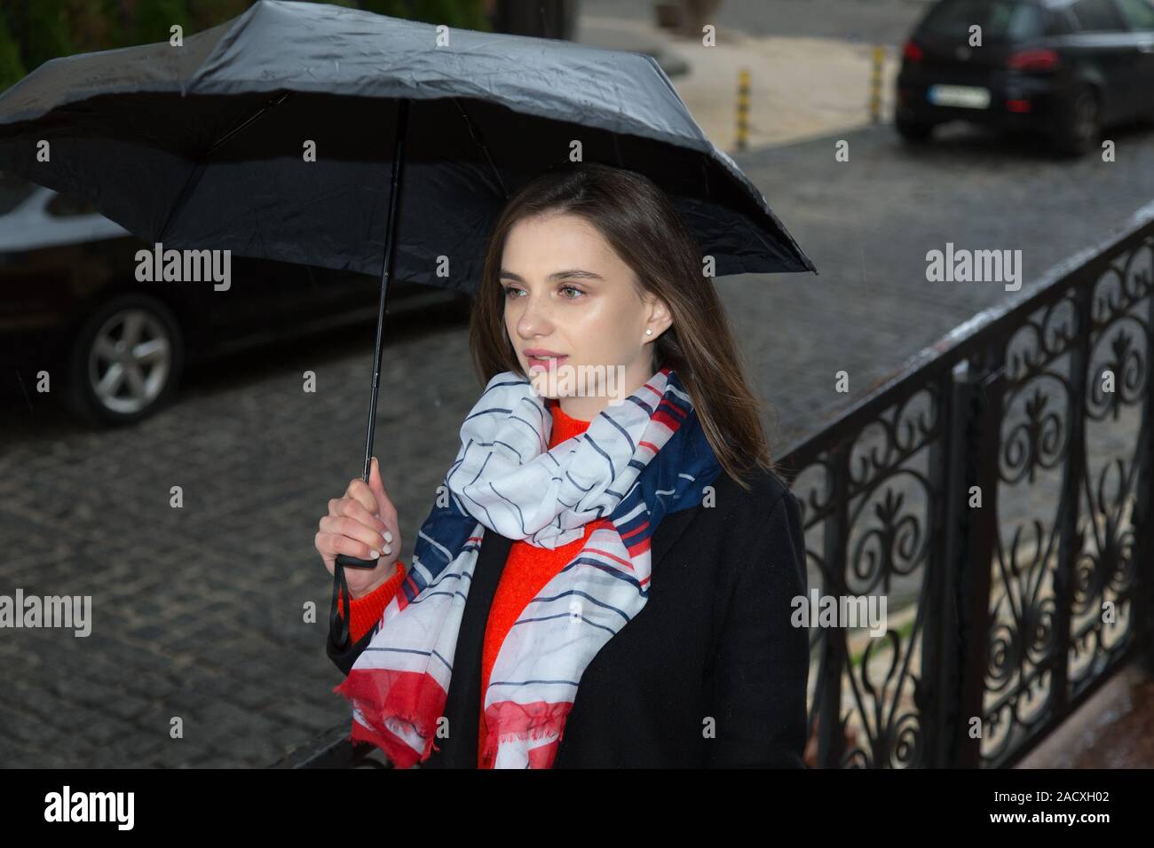 Portrait of young beautiful girl under a umbrella in rainy day. Happy young woman standing under umbrella in rain, laughing. Stock Photo