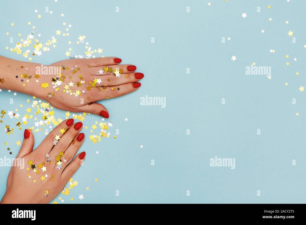 Woman hands with red manicure on blue background with golden stars sprinkles. Holiday, party and Christmas concept. Stock Photo