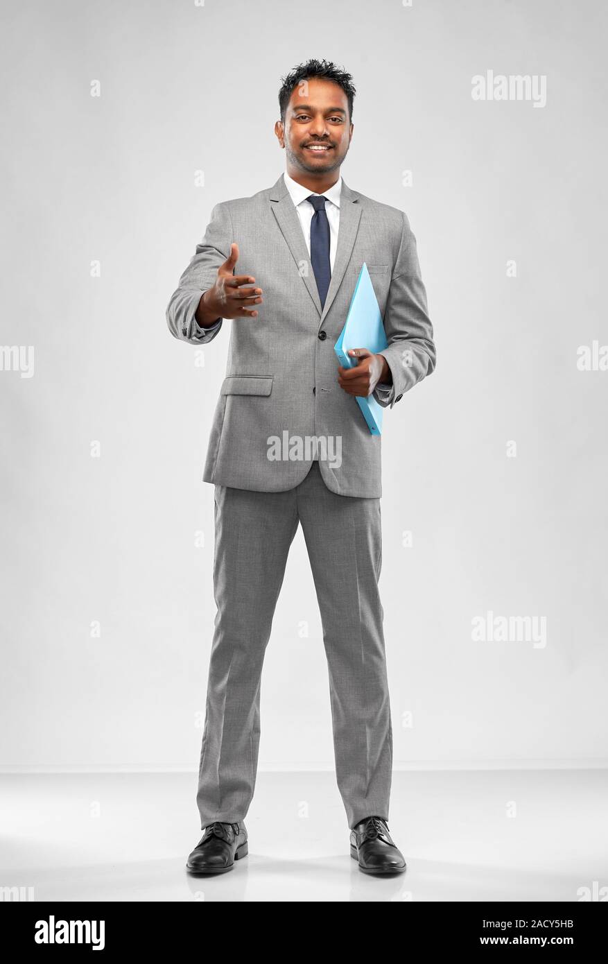 business, office worker and people concept - smiling indian businessman with folder stretching hand out for handshake over grey background Stock Photo