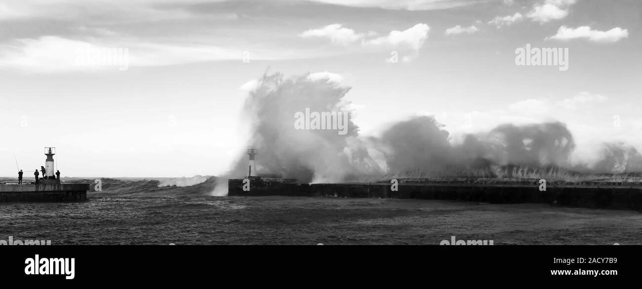 Waves crashing over lighthouse in Kalk Bay Harbour as fishermen brave storm, Cape Town, South Africa. Stock Photo