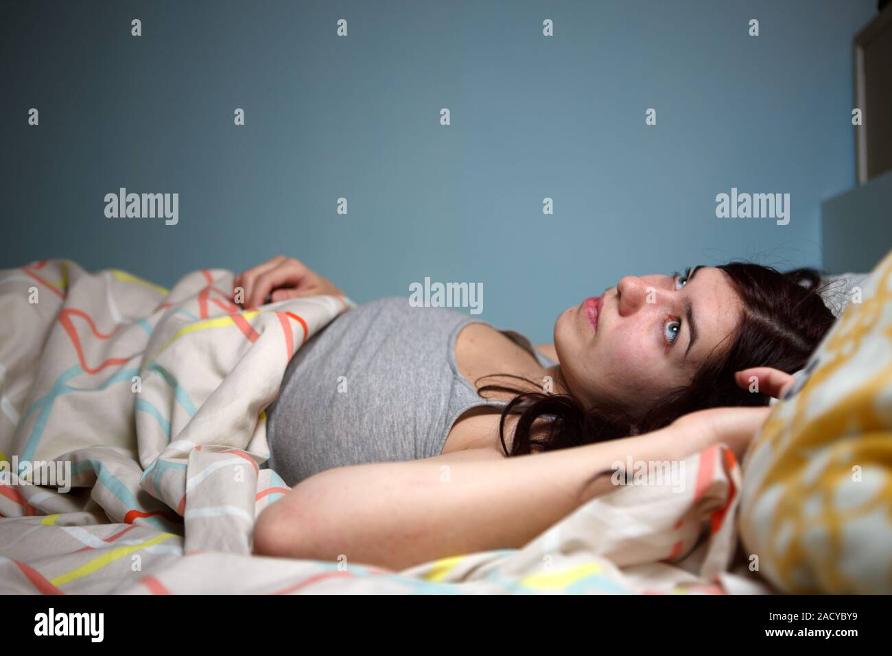 Young woman lying in bed suffering with insomnia  Noisy neighbour, stress, alarm sound, prevent from sleep concept Stock Photo