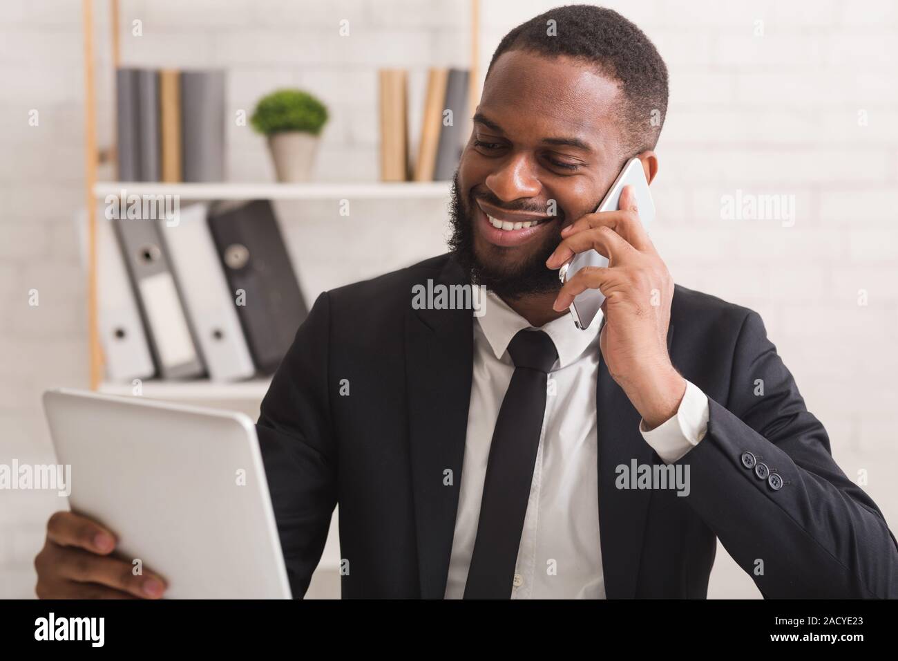 Cheerful businessman using tablet while talking by phone Stock Photo