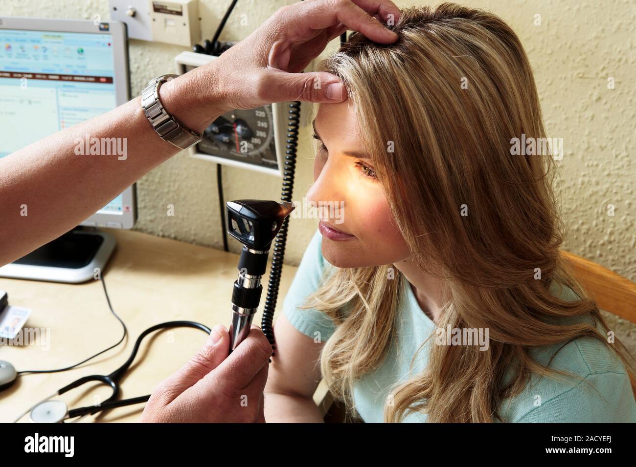 Eye examination. General practice doctor (GP) using an ophthalmoscope to examine a female