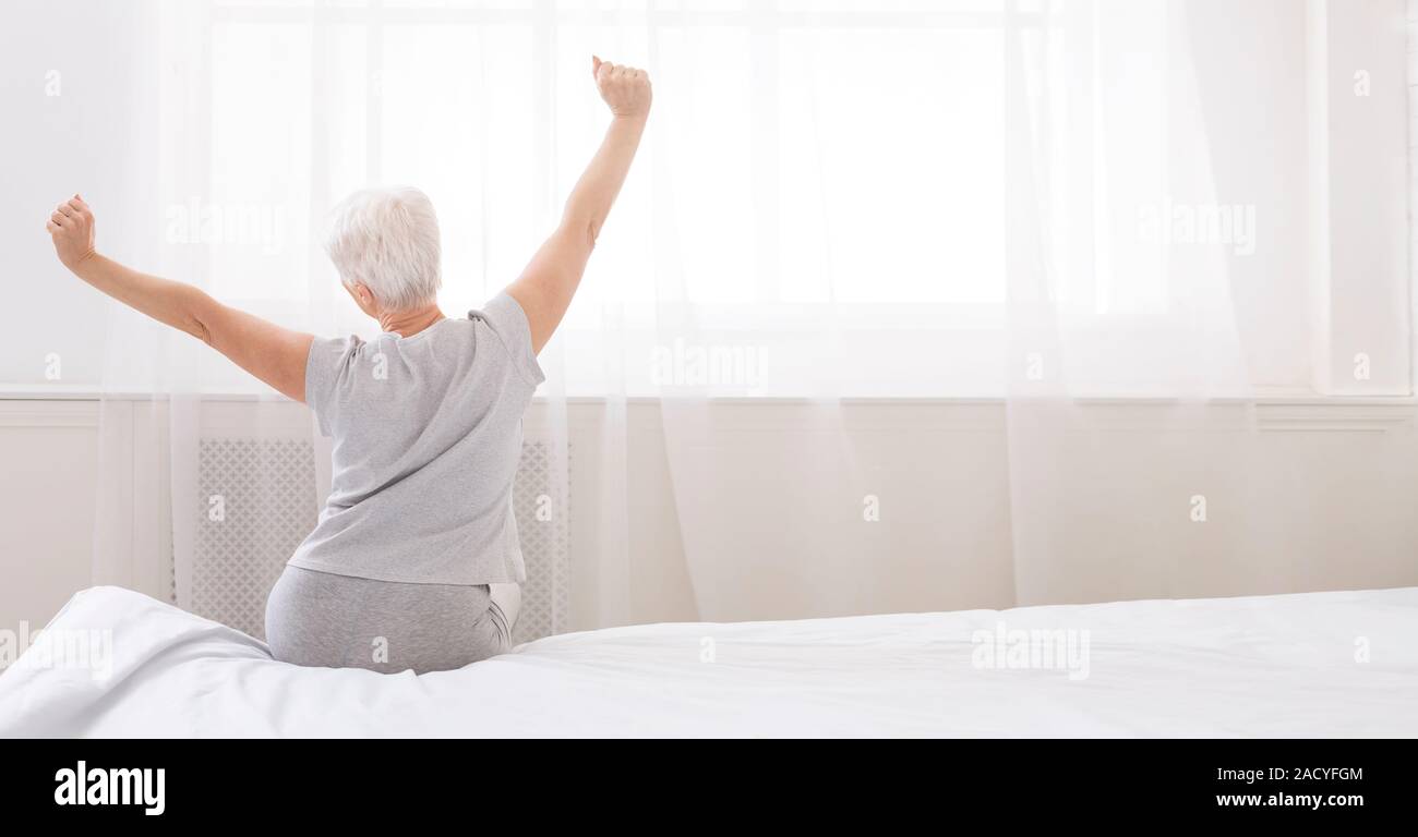 Well slept senior woman stretching with arms raised on bed Stock Photo