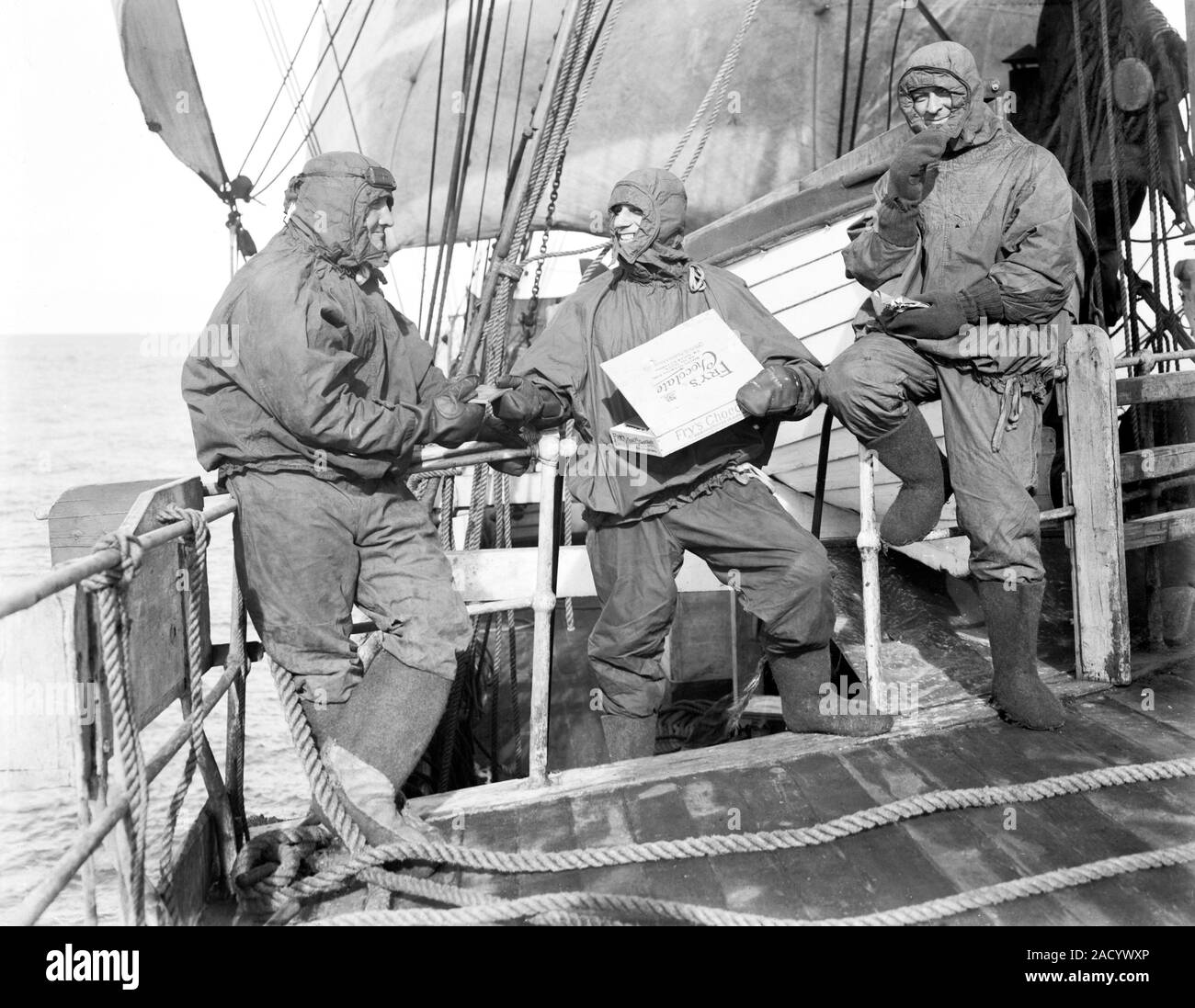 Fry's chocolate on Terra Nova. Expedition members in wet-weather gear eating Fry's chocolate on the deck of the Terra Nova as it sailed to Antarctica. Stock Photo
