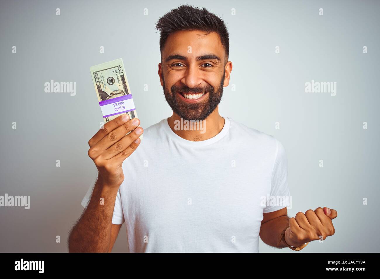 Young indian man holding dollars standing over isolated white ...