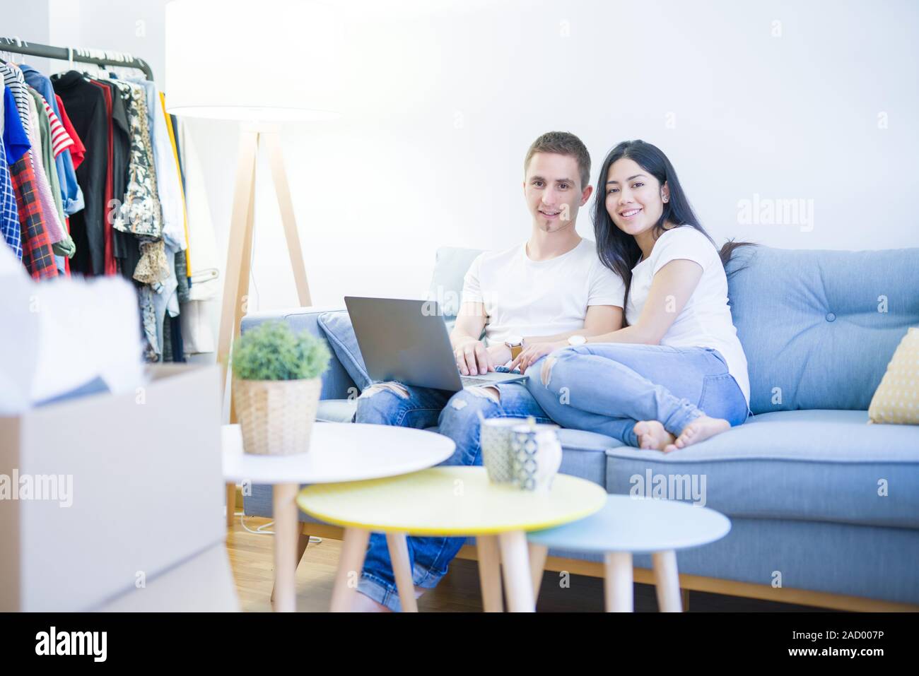 Young beautiful couple sitting on the sofa using laptop at new home ...