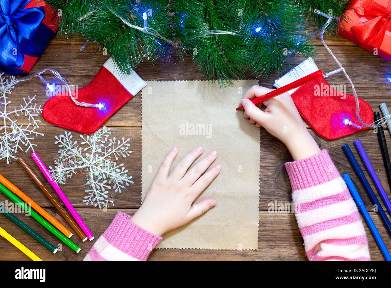 Children's letter to Santa Claus. Little girl writes a letter with multi-colored felt-tip pens on a wooden table with Christmas decorations on old Stock Photo