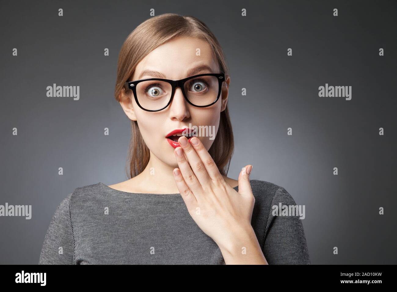 Wide-eyed astonished woman covering mouth with hand Stock Photo