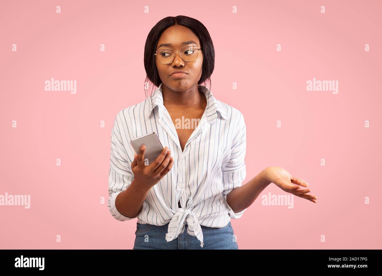Discontented Afro Woman Holding Smartphone Shrugging Shoulders, Pink Studio Background Stock Photo