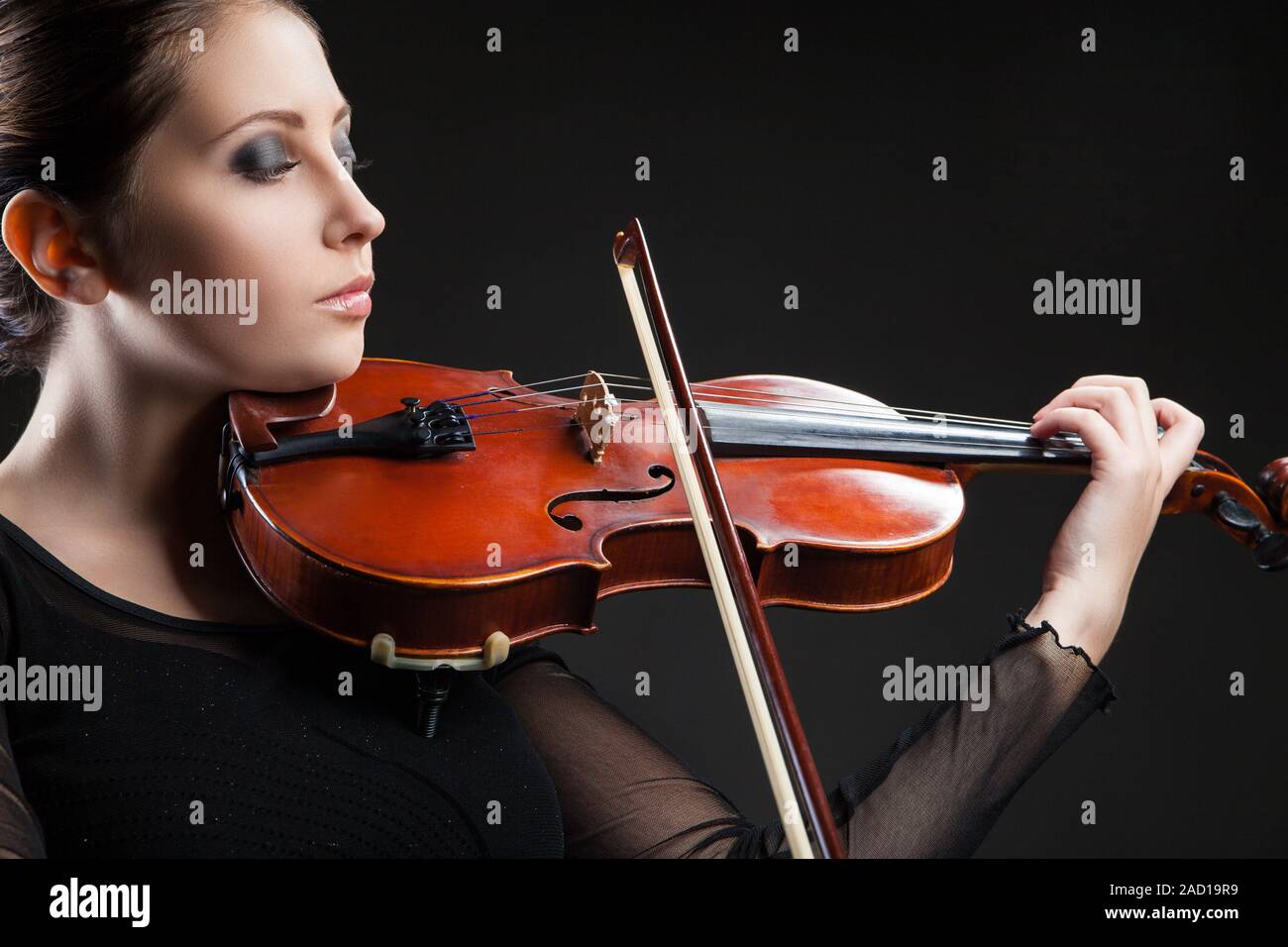 Beautiful young woman playing violin over black Stock Photo - Alamy