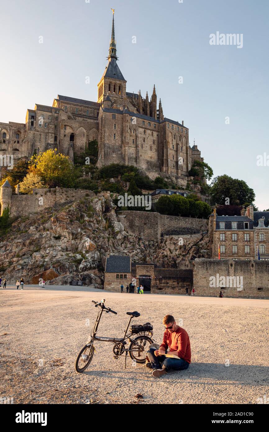 In the evening after the coach parties have left, this visitor finds some peace to read a book at Mont Saint-Michel, Normandy, France Stock Photo