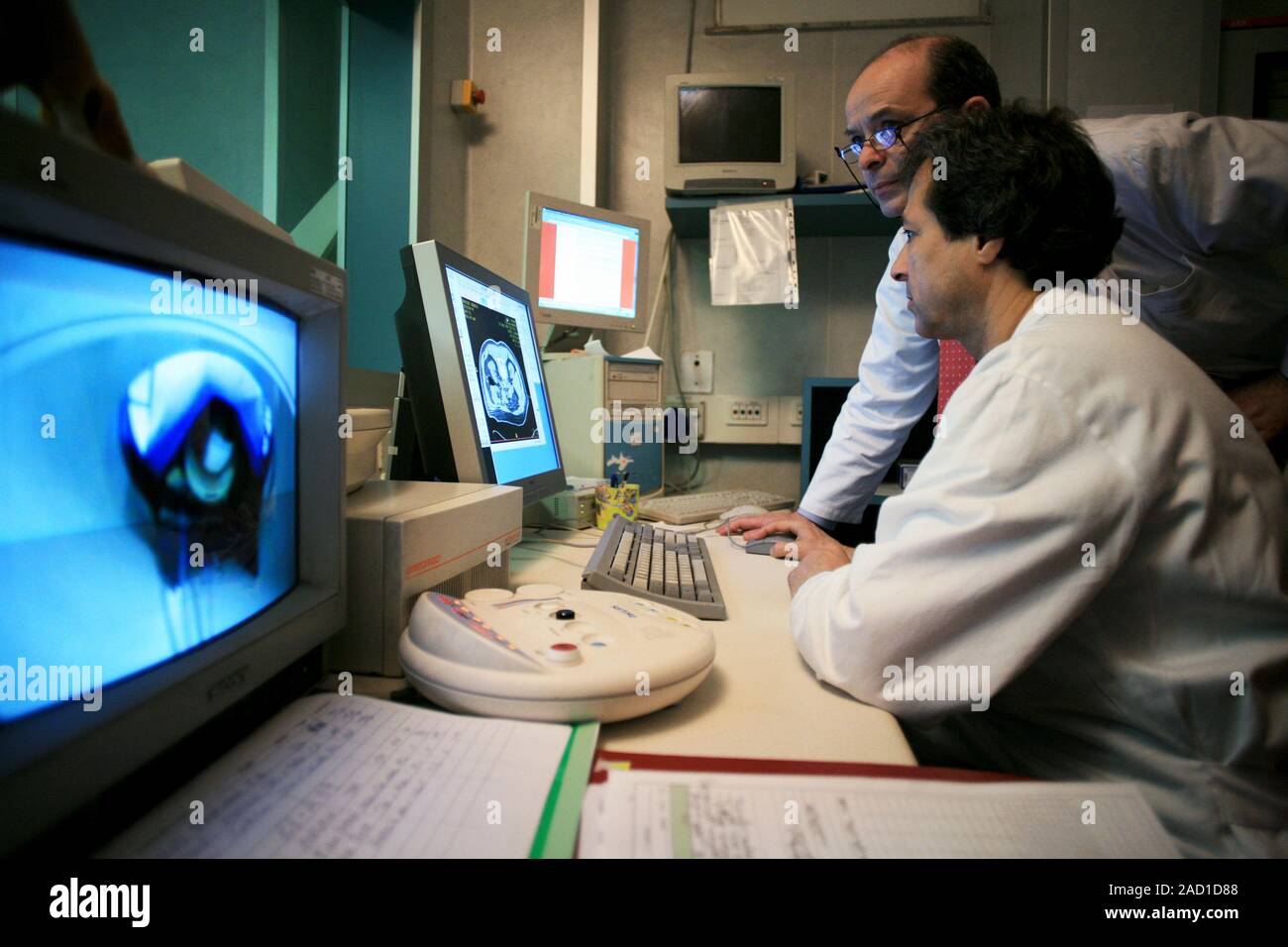 Advanced cancer treatment. Surgeons looking at a computed tomography (CT) scan while operating on a patient (in scanner on screen at left). They are u Stock Photo
