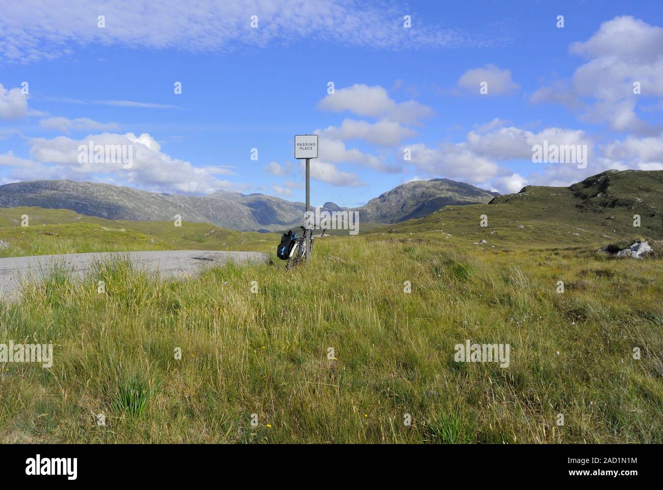 A laden touring bike leans against a passing place sign on a remote single-track road by Nedd, Highland, Scotland Stock Photo