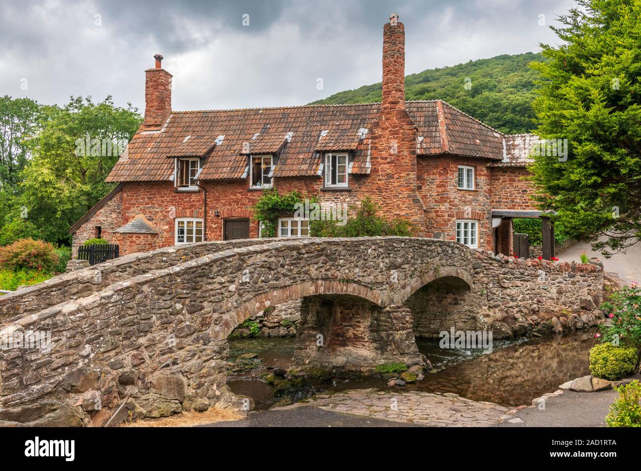 Hidden away, not far from the village of Porlock in rural Somerset, a bridge crosses a stream leading to a picturesque cottage and woodland beyond. Stock Photo