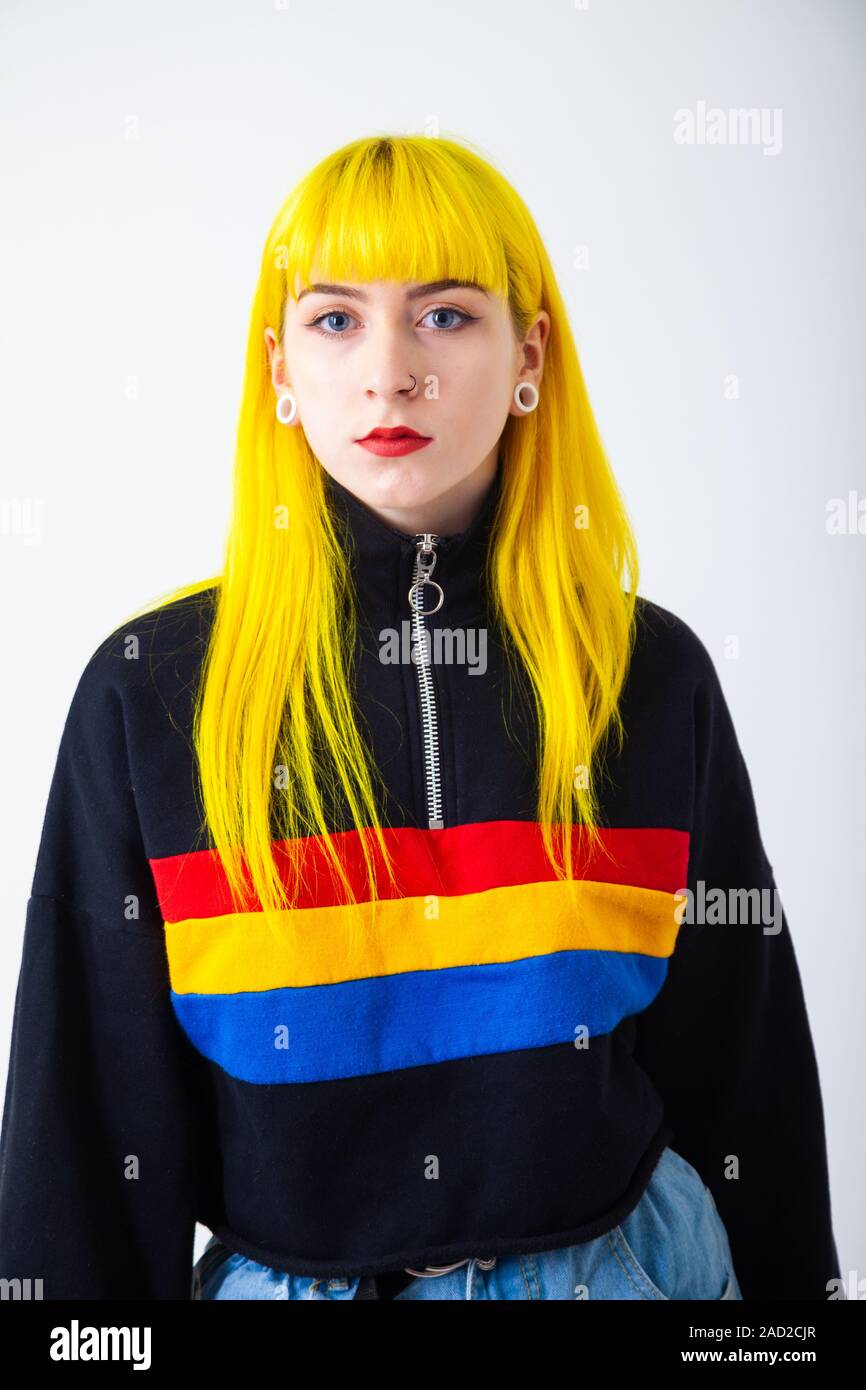 A young woman with bright yellow hair wearing a colourful top against a white background Stock Photo