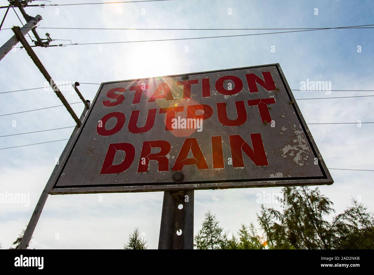 low angle view of a white and red sign against the sky, electric towers and cables, STATION, OUTPUT, DRAIN, Electrical substation Signage Stock Photo