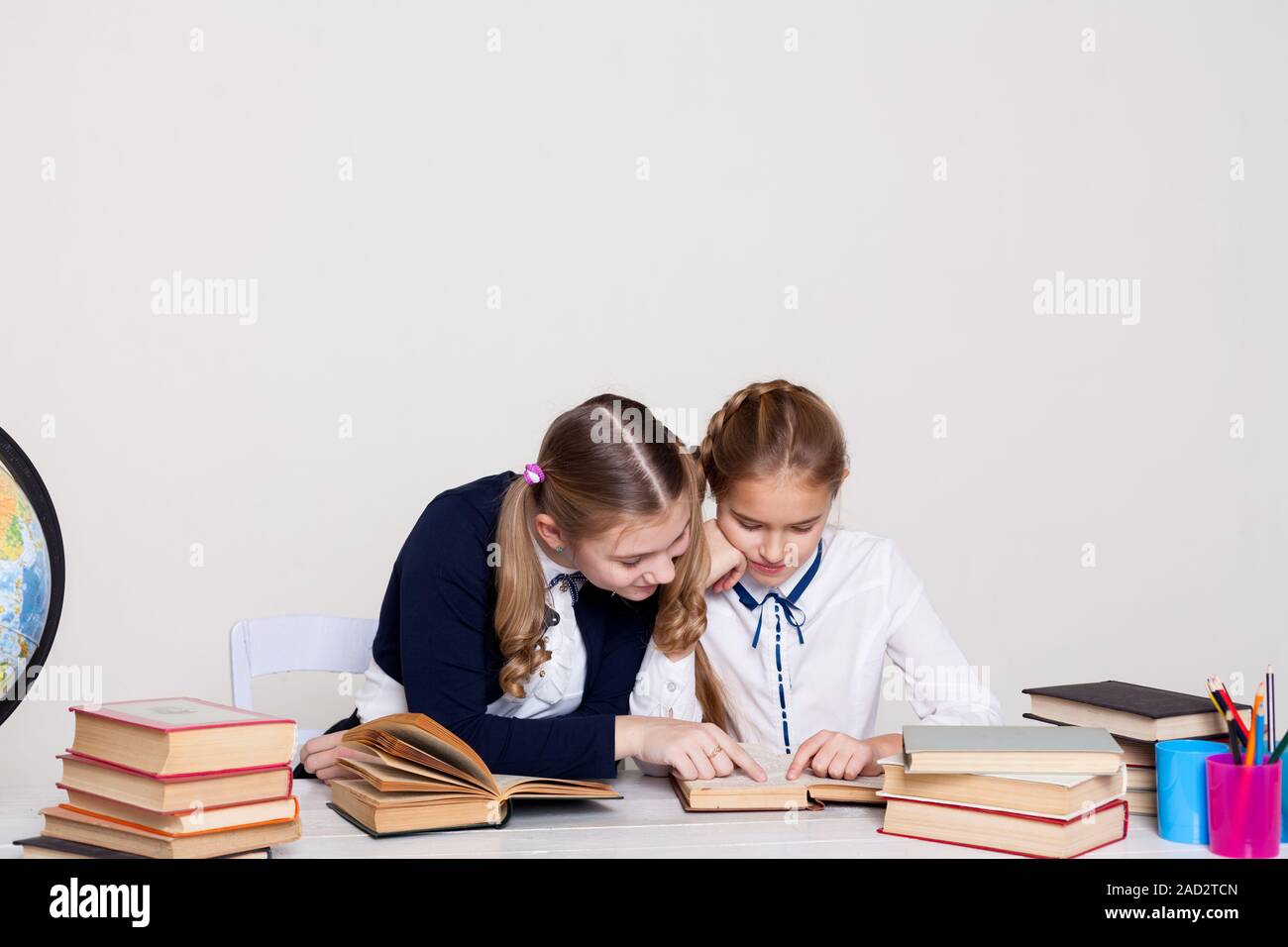 two girls of the school with books for studying sit at the desk in the ...