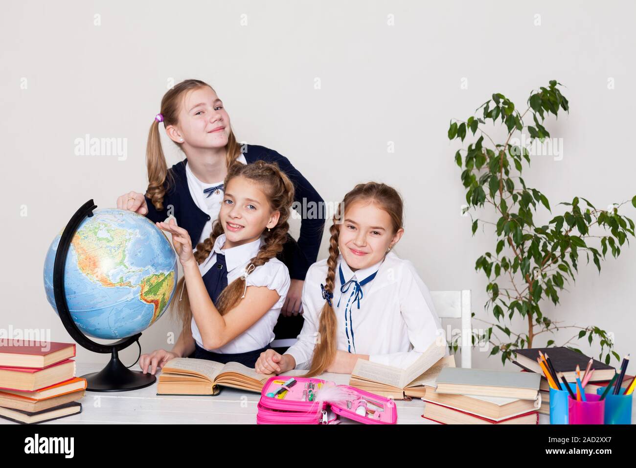 three girls of the school with books for studying sit at the desk in ...