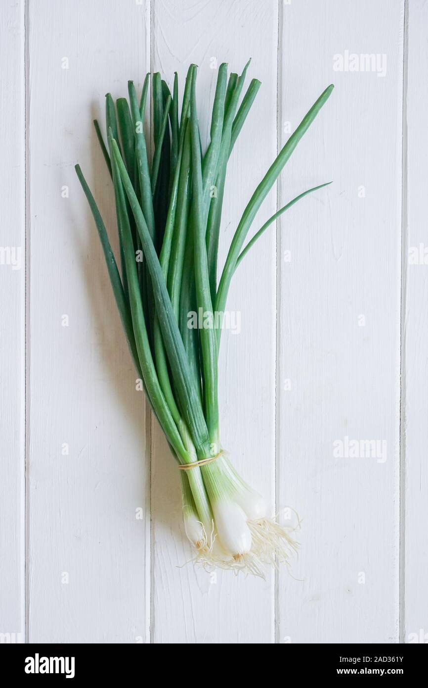 bundle of scallions or spring onions, top view on white wooden table Stock Photo